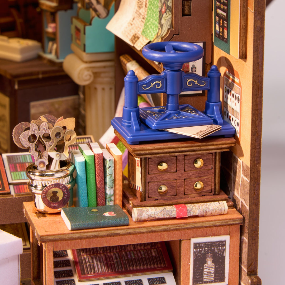 Detaljefoto af Rolife Wisdom Stationery Shop – blå miniature bogpresse på træskuffemøbel med små bøger og nøgler
